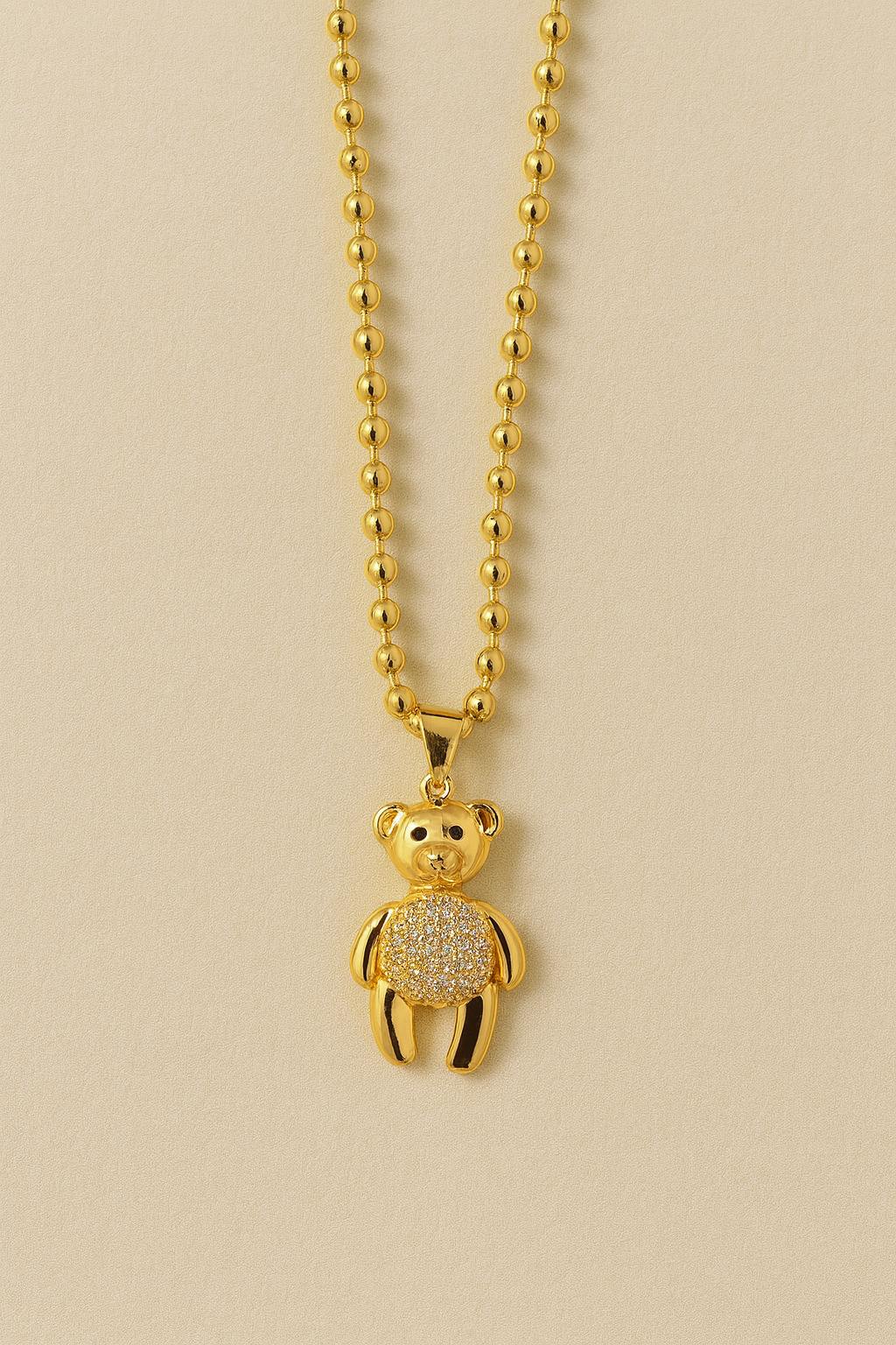 A gold tone teddy pendant necklace featuring a polished silhouette with a sparkling crystal-accented body.